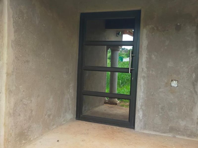 An unfinished entrance area featuring a modern aluminium glass door, exposed brickwork, and raw plastered walls awaiting final finishes.