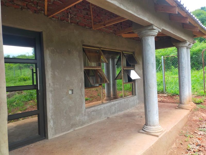 An unfinished covered patio area featuring concrete columns, exposed brickwork, and metal-framed windows, awaiting final exterior finishes and ceiling installation.