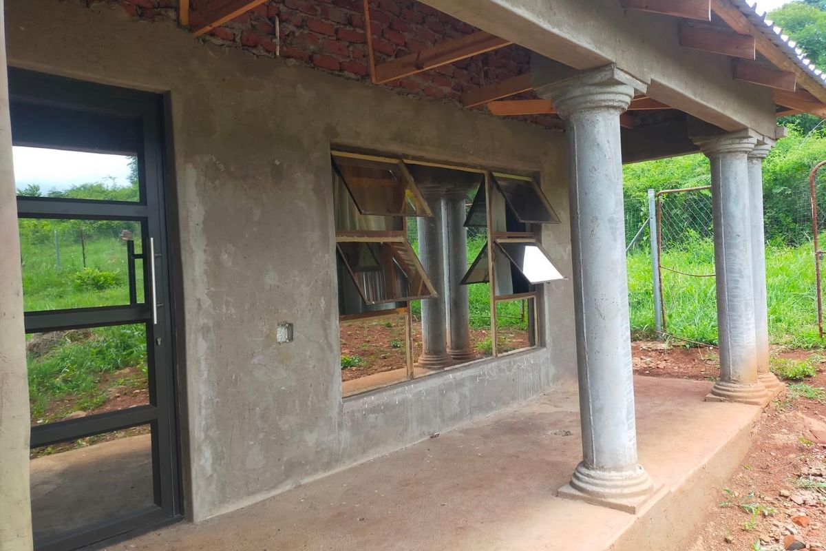 An unfinished covered patio area featuring concrete columns, exposed brickwork, and metal-framed windows, awaiting final exterior finishes and ceiling installation.