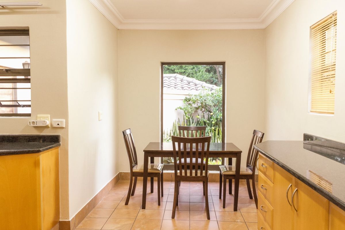 A functional kitchen dining area featuring wooden cabinetry, dark granite countertops, tiled flooring, and natural light from multiple windows.