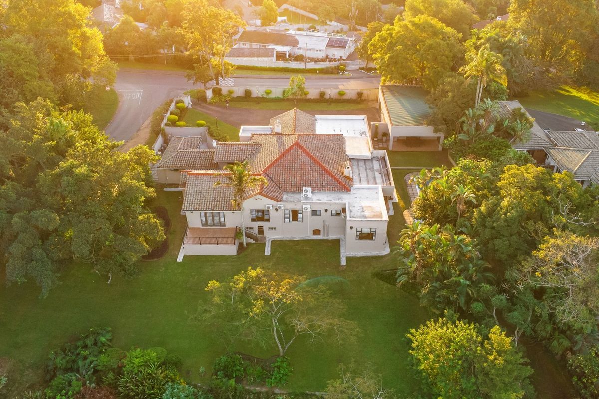 Aerial view of a residential property featuring a tiled roof, expansive garden, and surrounding mature trees in a quiet neighborhood setting.