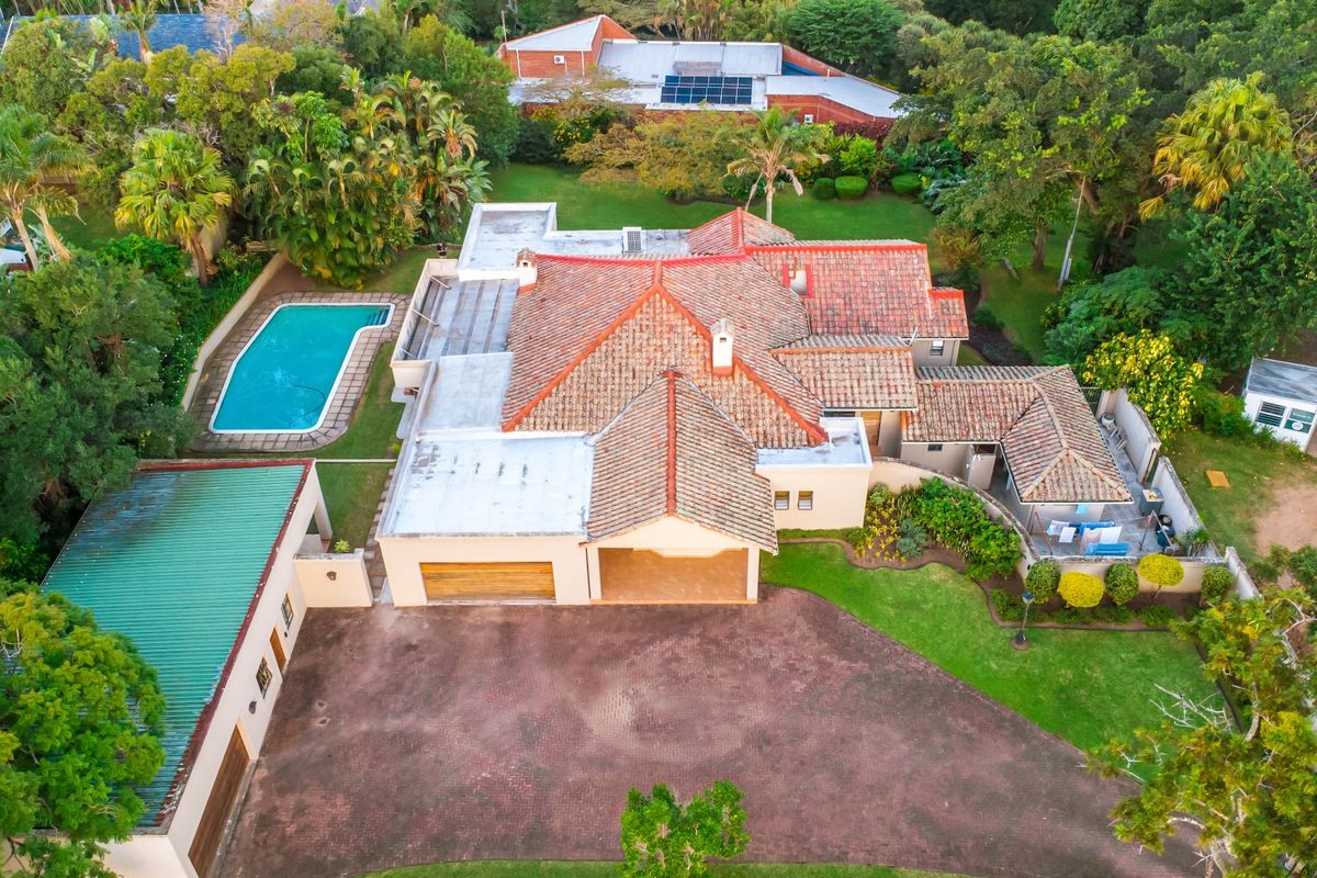 Aerial view of a residential property featuring a tiled roof, swimming pool, expansive garden, paved driveway, and a detached garage structure.