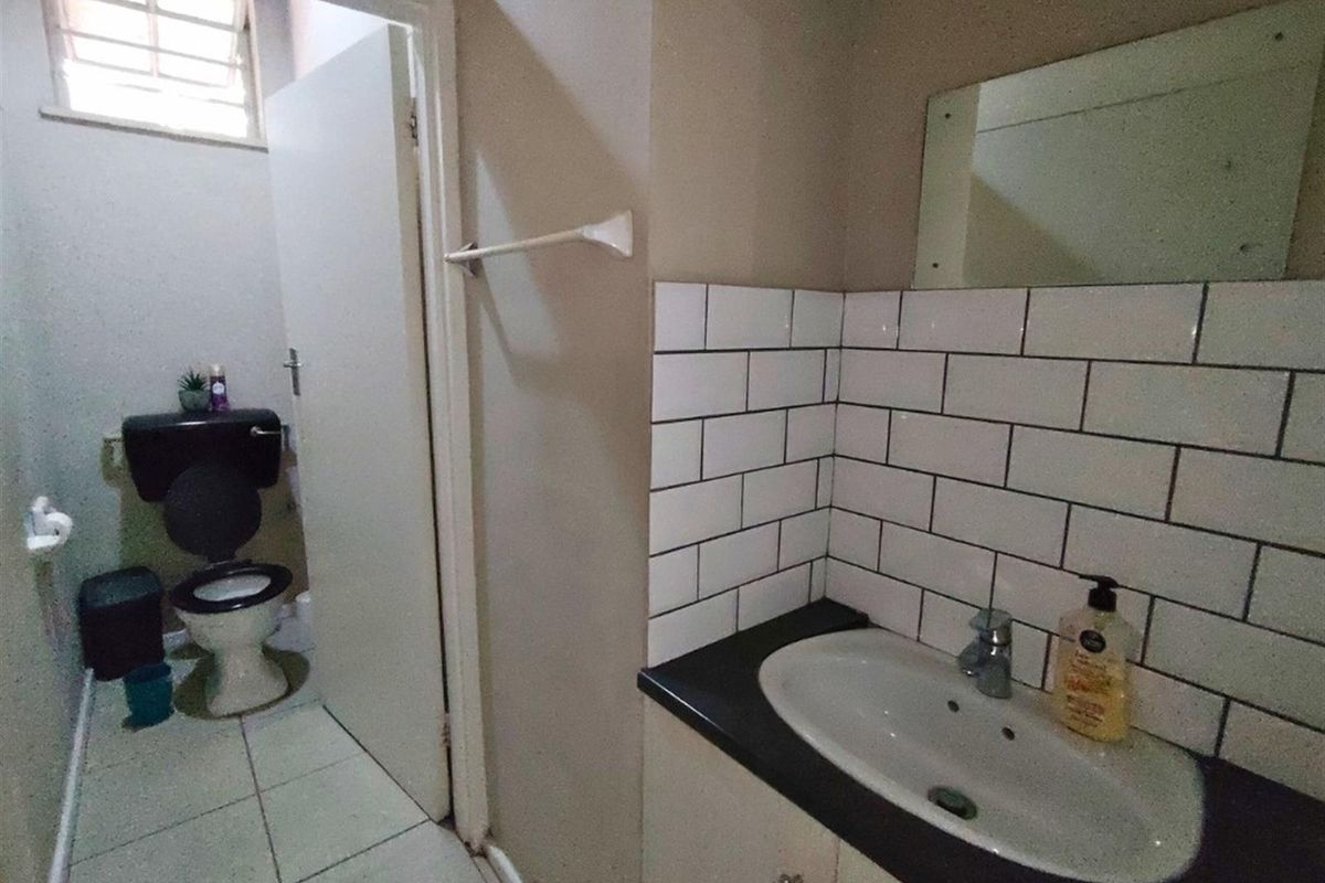 A functional bathroom featuring a vanity with a basin, subway tile backsplash, and a separate toilet area with a window for ventilation.