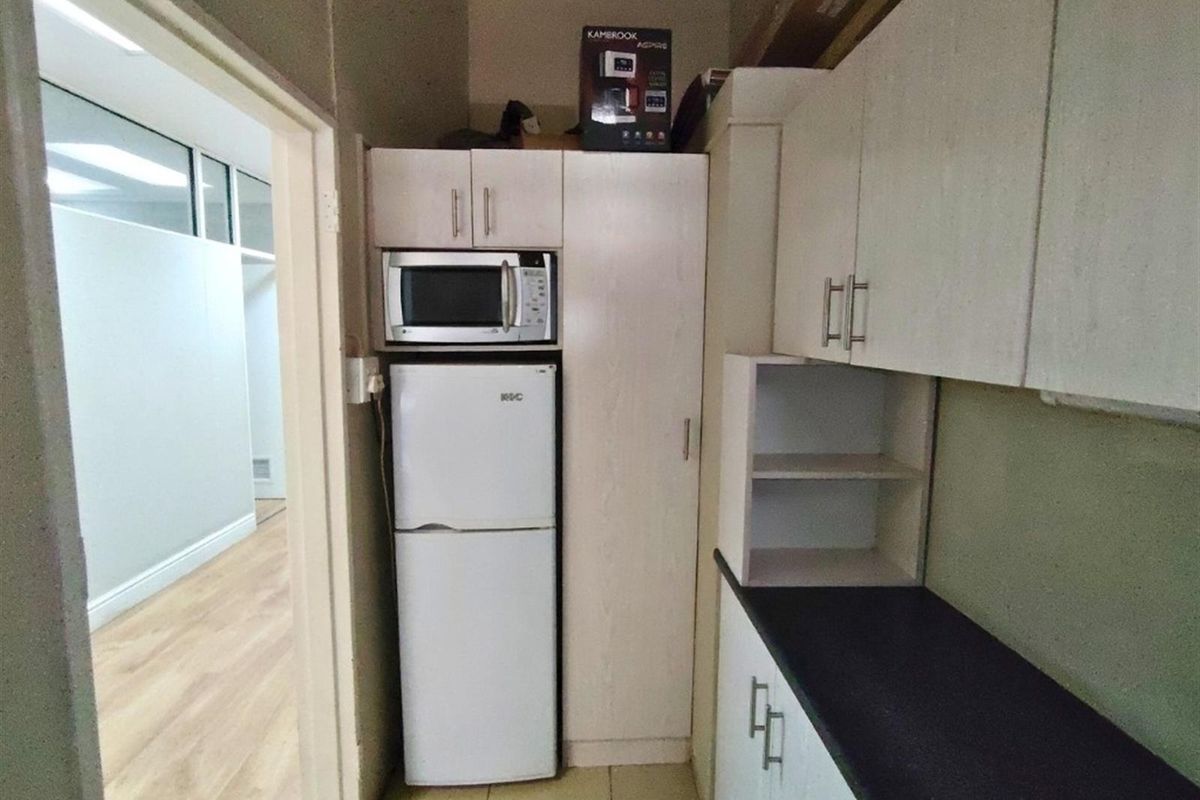 A compact kitchenette area featuring built-in cabinetry, a dark countertop, and integrated storage space, adjacent to a hallway.