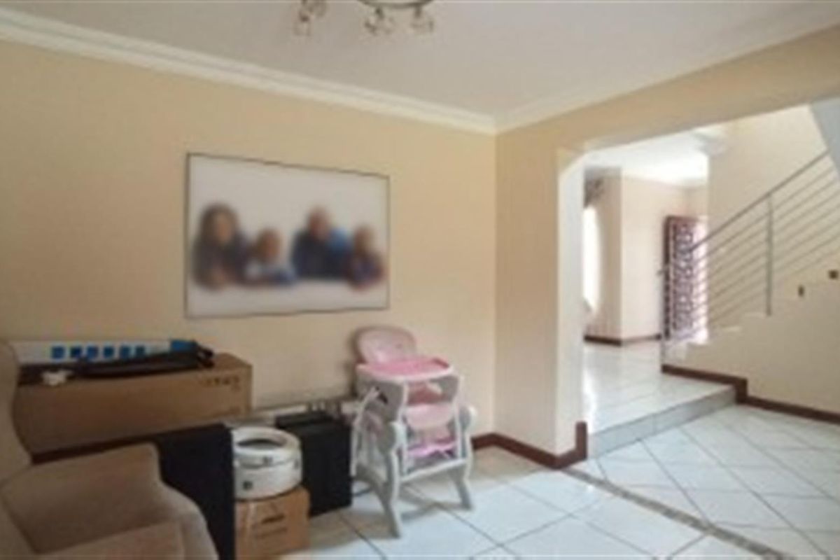 An interior view of a living area featuring tiled flooring and an open transition to a staircase with a metal railing.