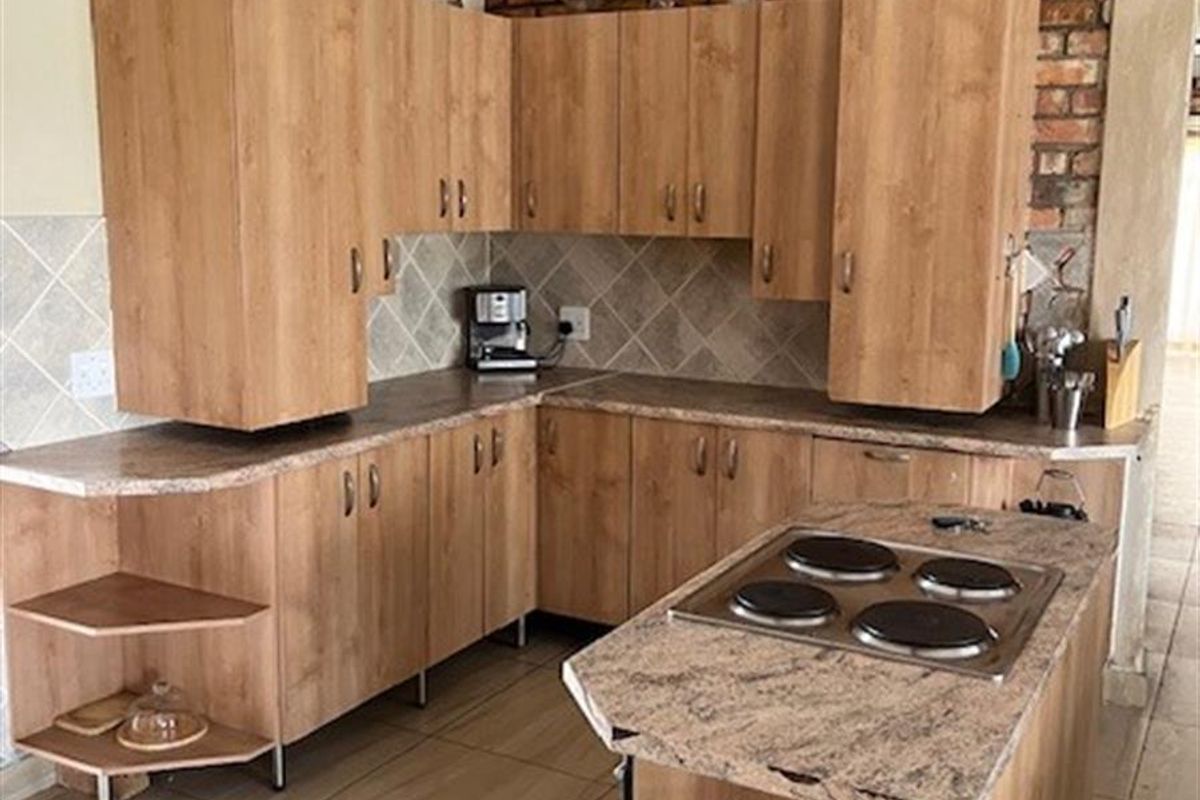 A kitchen featuring wood-look cabinetry, stone-effect countertops, a built-in electric hob, and a rustic exposed brick feature wall under a vaulted ceiling.