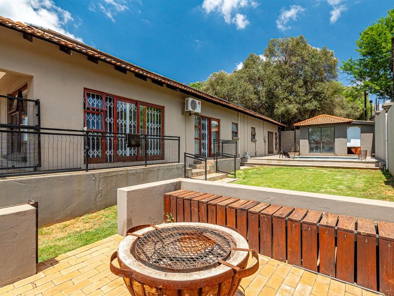 Rear exterior view featuring a paved patio with a built-in braai, a swimming pool, and a landscaped garden area.