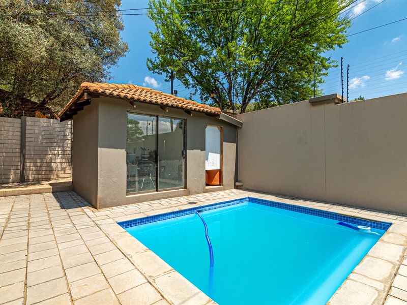 Outdoor pool area featuring a tiled surround, perimeter wall with electric fencing, and a small outbuilding with a tiled roof.