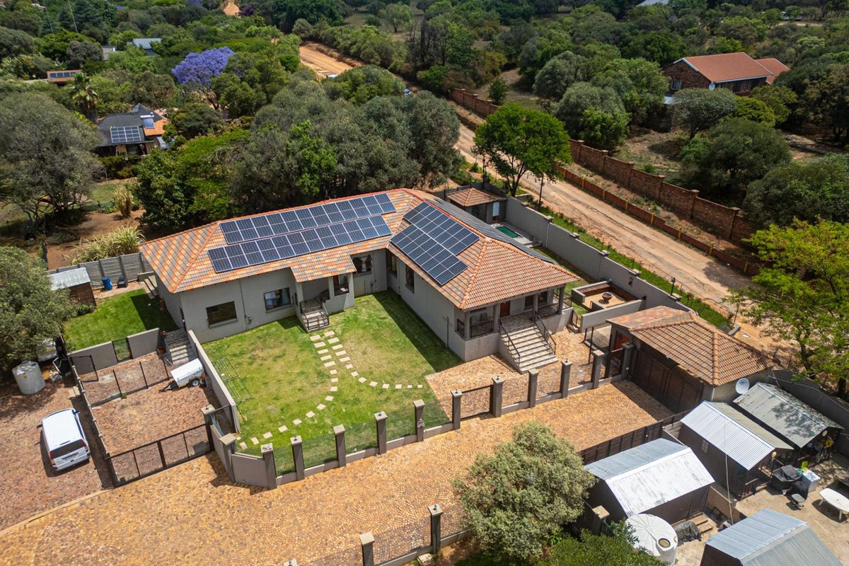 Aerial view of a residential property featuring a tiled roof with solar panels, a paved driveway, a landscaped lawn, and perimeter walling.