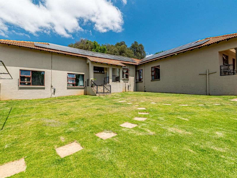 Rear view of the property featuring a large lawn, stepped stone pathway, and solar panels installed on the tiled roof.
