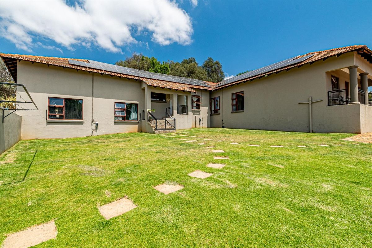 Rear view of the property featuring a large lawn, stepped stone pathway, and solar panels installed on the tiled roof.