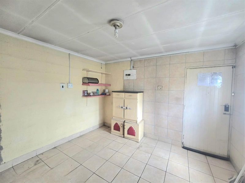 A basic utility or kitchen area featuring tiled flooring, wall tiling, and exposed electrical infrastructure, requiring significant cosmetic updates and maintenance.