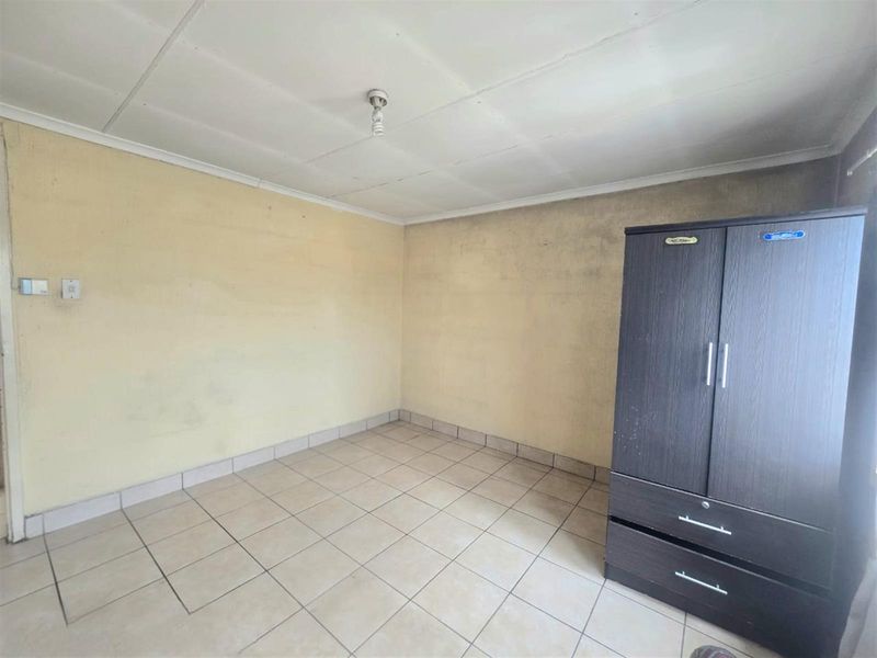 A basic bedroom featuring tiled flooring and plain walls, requiring cosmetic updates and maintenance to improve its overall condition.