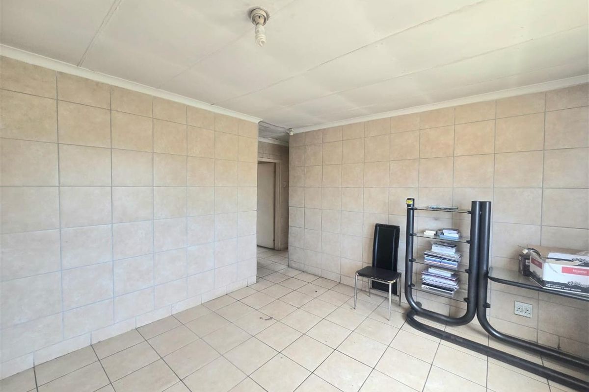 A sparsely furnished living area featuring tiled walls and flooring throughout, offering a blank canvas for renovation or interior design updates.