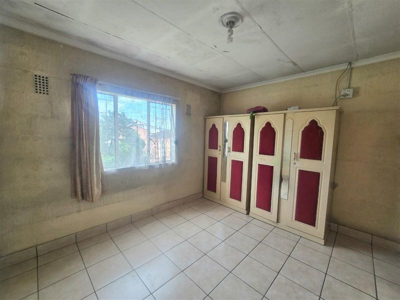 A bedroom featuring tiled flooring, a window with security bars, and a built-in wardrobe, requiring cosmetic updates and repairs to the walls and ceiling.
