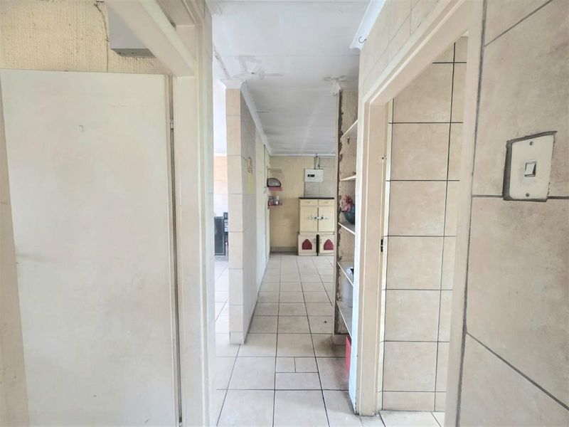 A narrow interior hallway featuring tiled flooring and access to adjacent rooms, showing signs of wear and requiring cosmetic updates.