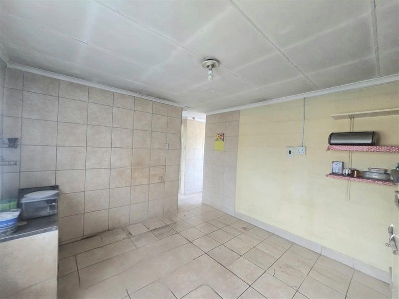 A basic kitchen area featuring tiled walls and flooring, with simple shelving and basic electrical fixtures, requiring cosmetic updates.