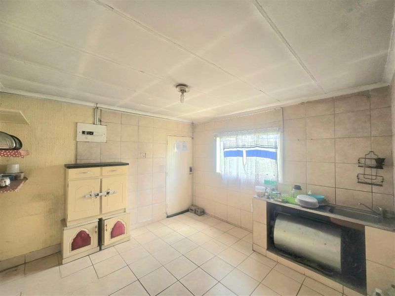 A functional kitchen space featuring tiled walls and flooring, a built-in sink area, and basic cabinetry, offering potential for modernization and renovation.