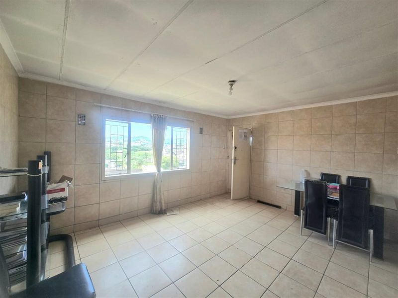 A tiled living area featuring large windows with natural light, offering a functional space with potential for modernization and cosmetic updates.