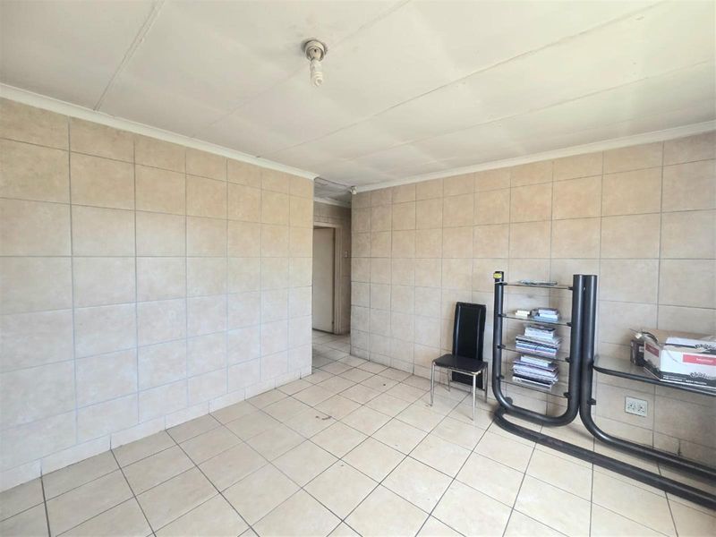 A sparsely furnished living area featuring tiled walls and flooring throughout, offering a blank canvas for renovation or interior design updates.