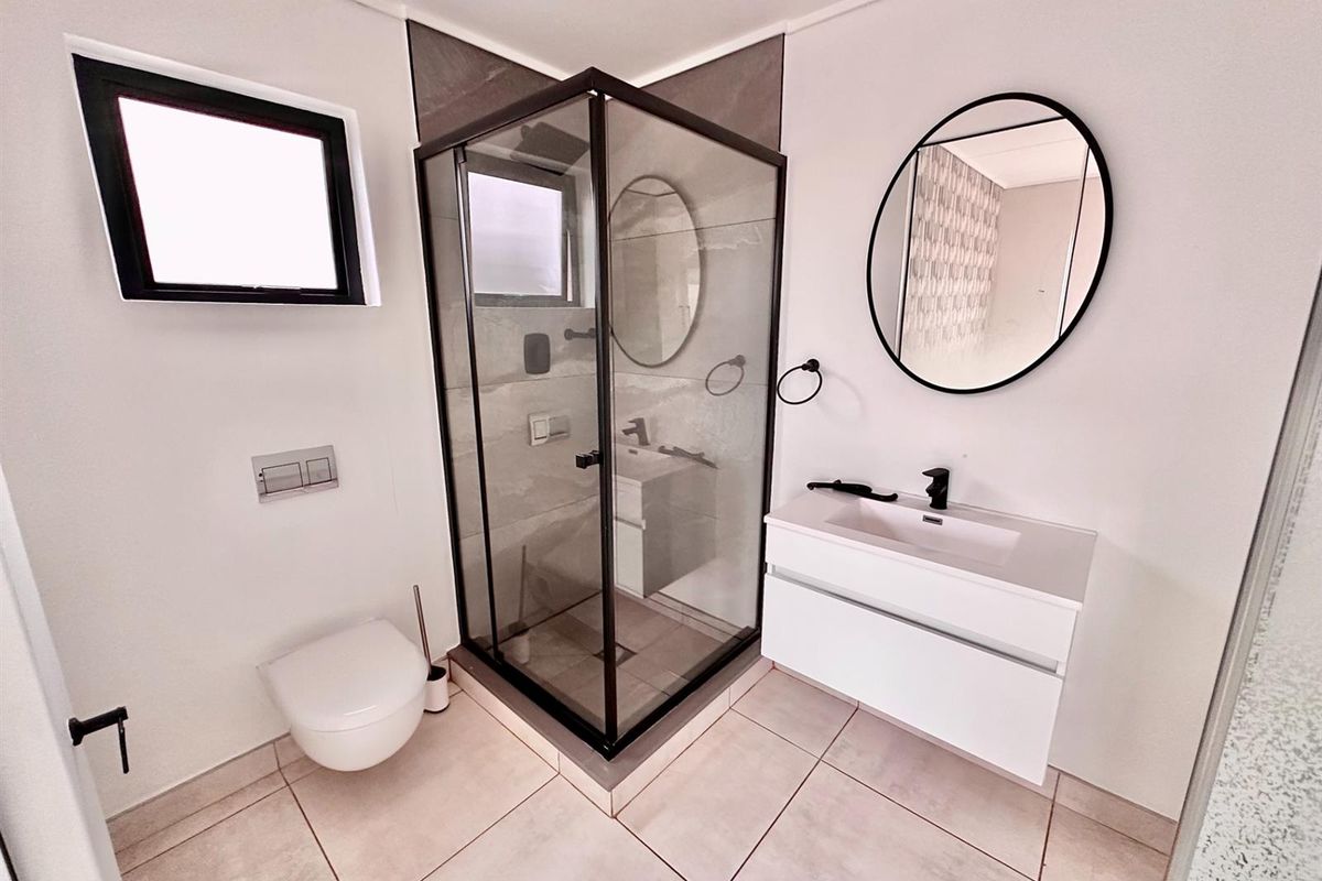 Modern bathroom featuring a wall-mounted vanity, a glass-enclosed corner shower with black framing, and a wall-hung toilet with concealed cistern.