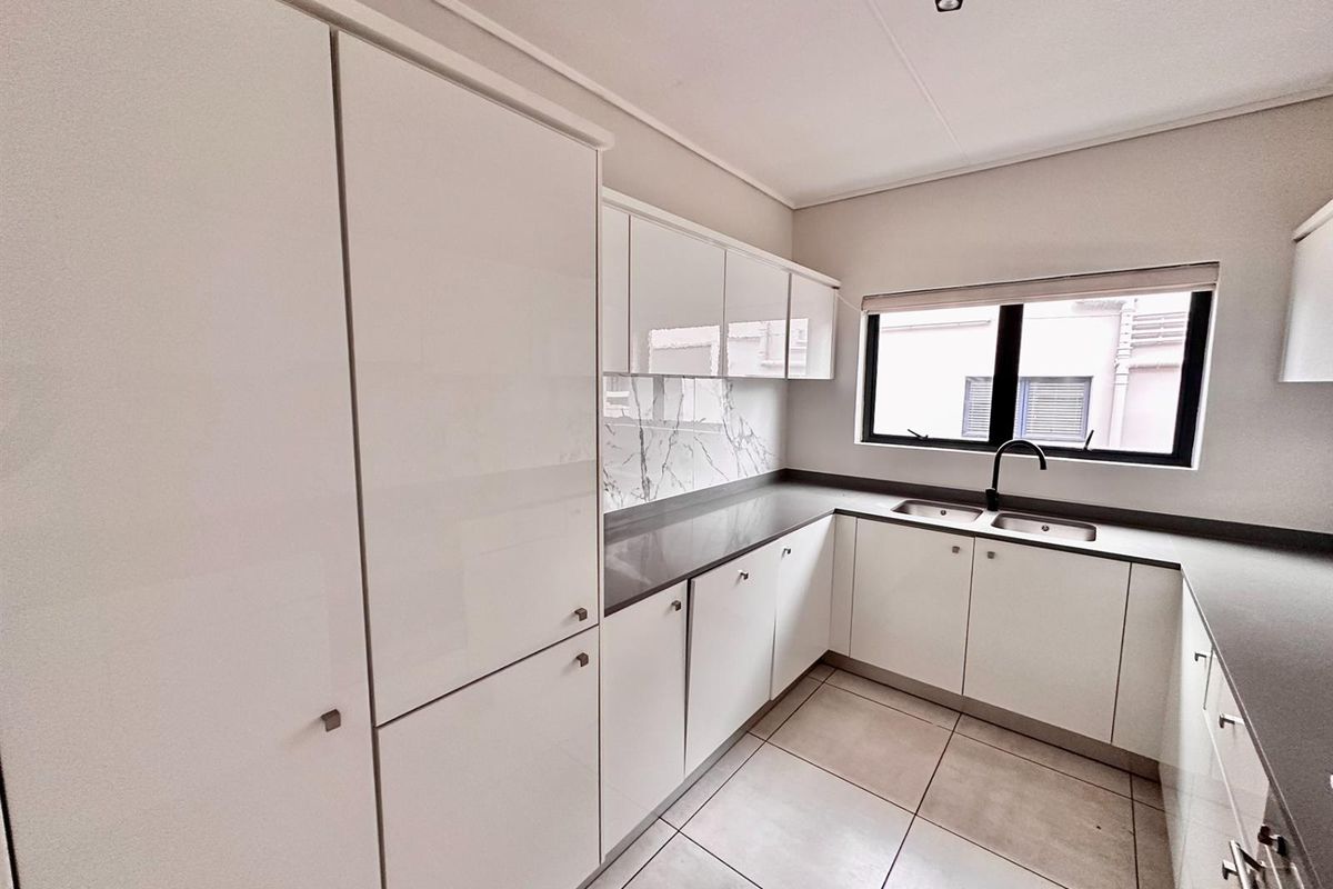 Modern kitchen featuring white high-gloss cabinetry, dark stone countertops, marble-look splashback, and a double-basin sink with a contemporary black faucet.