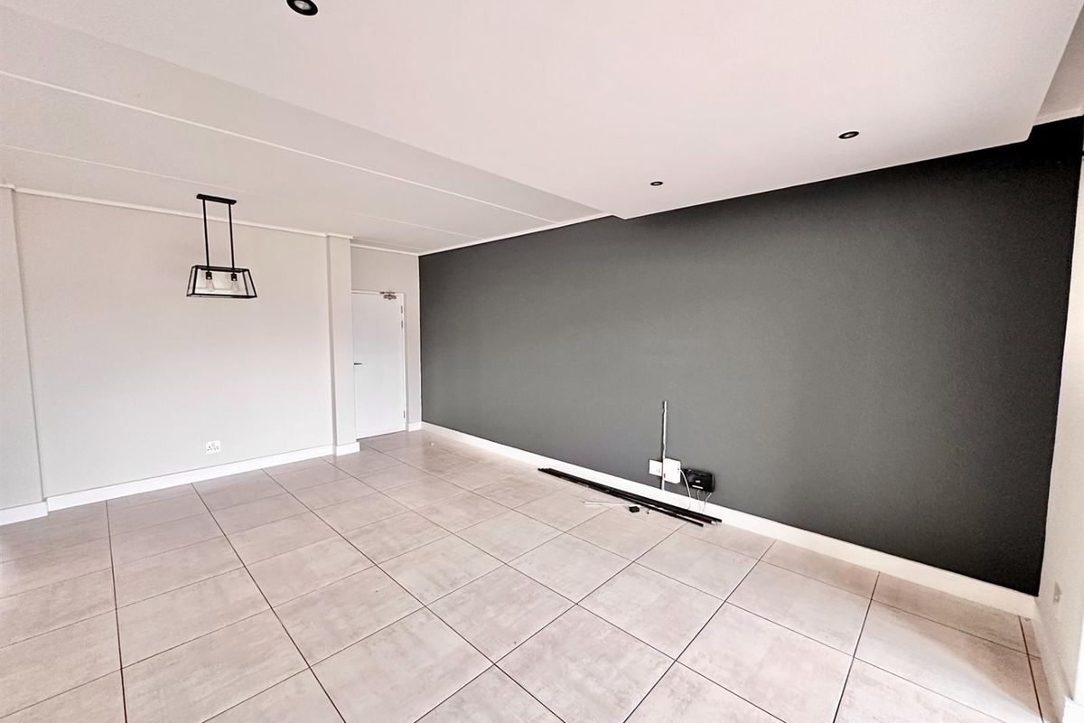A spacious, empty living area featuring neutral tiled flooring, a modern dark grey feature wall, and recessed ceiling lighting.