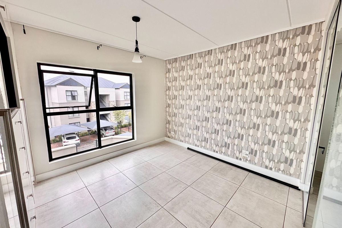 A bright, empty bedroom featuring large black-framed windows, neutral floor tiles, and a decorative patterned feature wall.