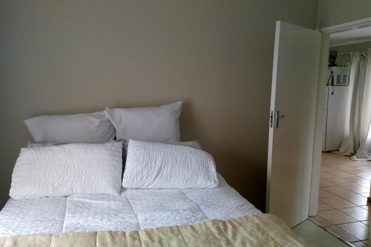 A bedroom featuring neutral wall tones and tiled flooring, with an open doorway leading to an adjacent living area.