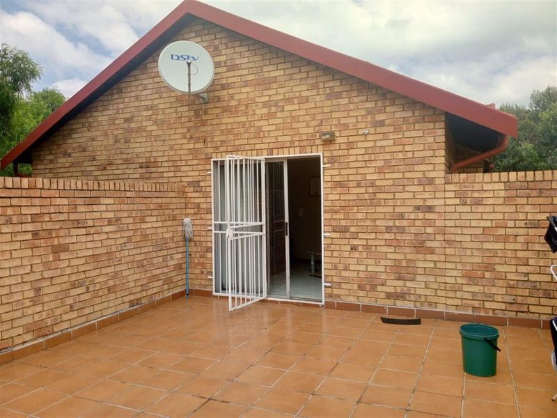 A private rear patio area featuring terracotta-style tiling, exposed brick walls, and a secure metal security gate leading into the home.