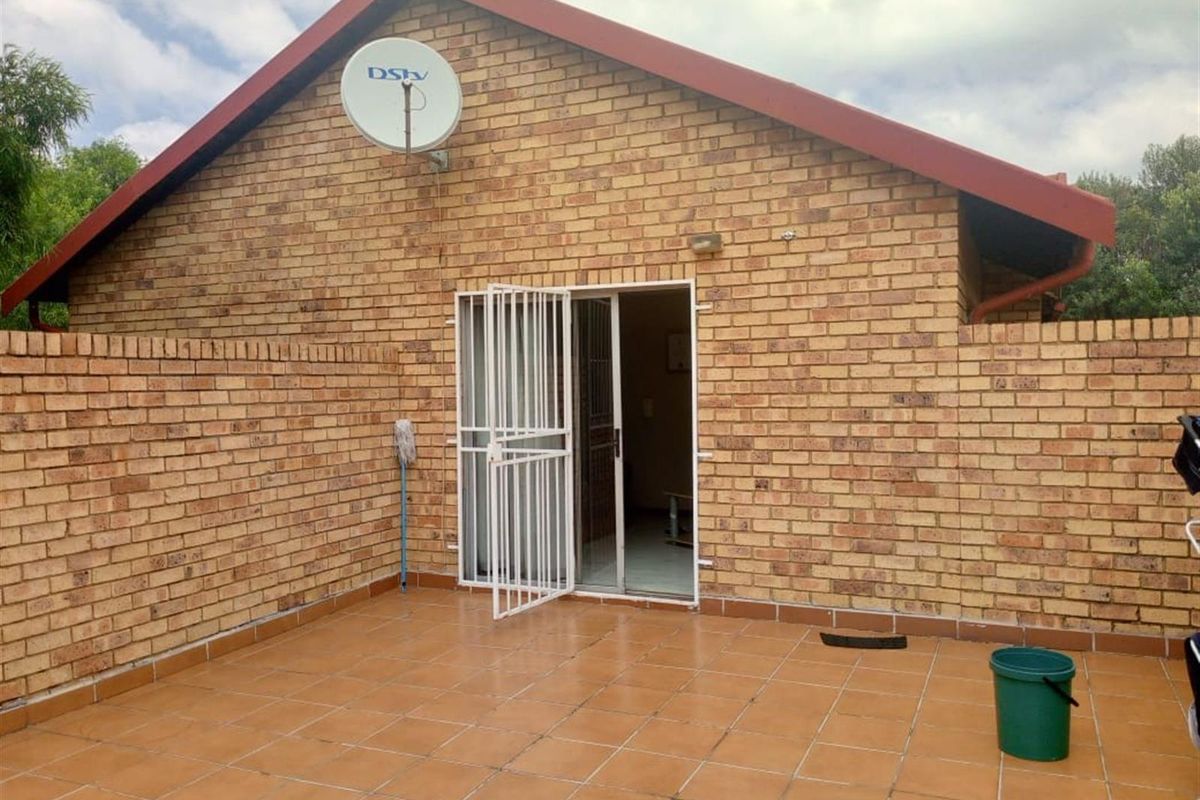A private rear patio area featuring terracotta-style tiling, exposed brick walls, and a secure metal security gate leading into the home.