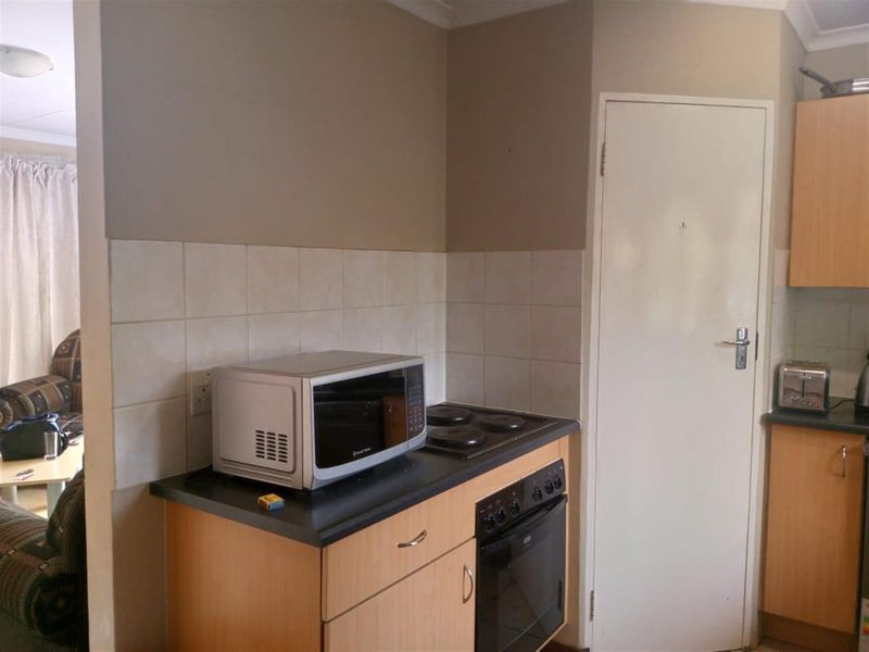 A functional kitchen area featuring light wood-tone cabinetry, a built-in electric oven and hob, and a tiled splashback.