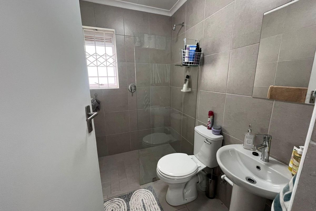 A modern bathroom featuring a glass-enclosed walk-in shower, pedestal basin, and toilet with neutral wall tiling.