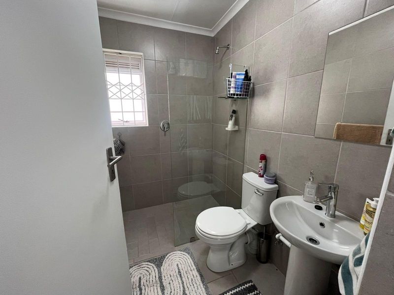 A modern bathroom featuring a glass-enclosed walk-in shower, pedestal basin, and toilet with neutral wall tiling.