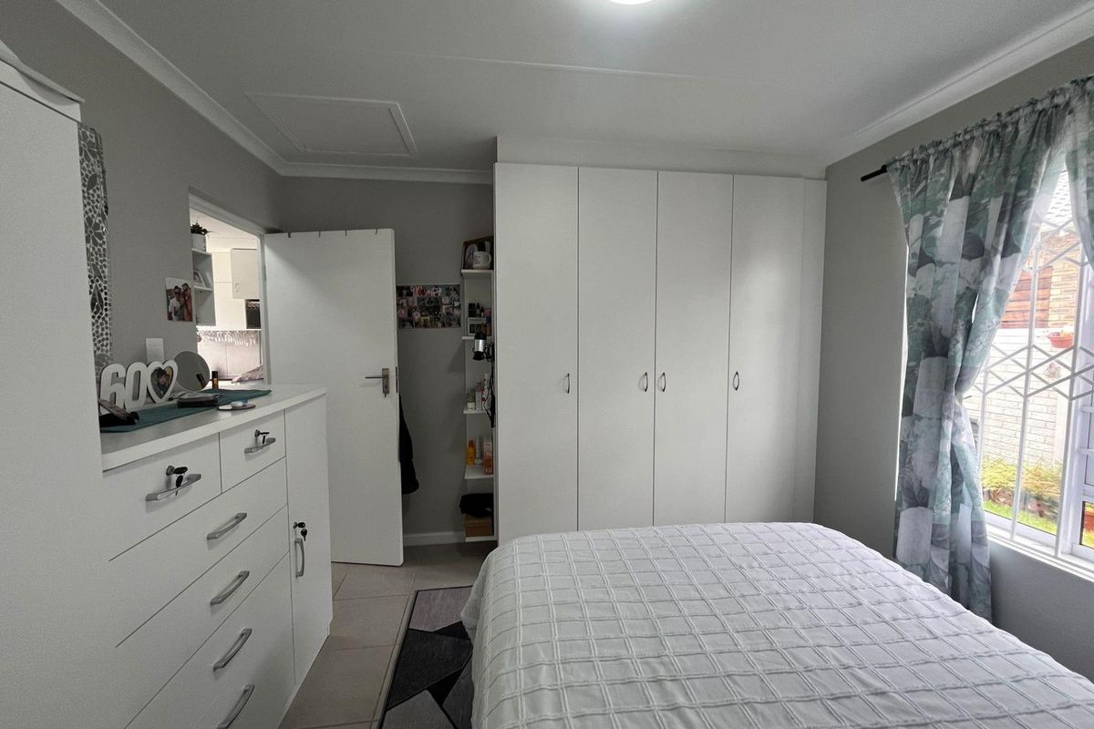 A well-maintained bedroom featuring built-in floor-to-ceiling wardrobes, tiled flooring, and a window with security bars.