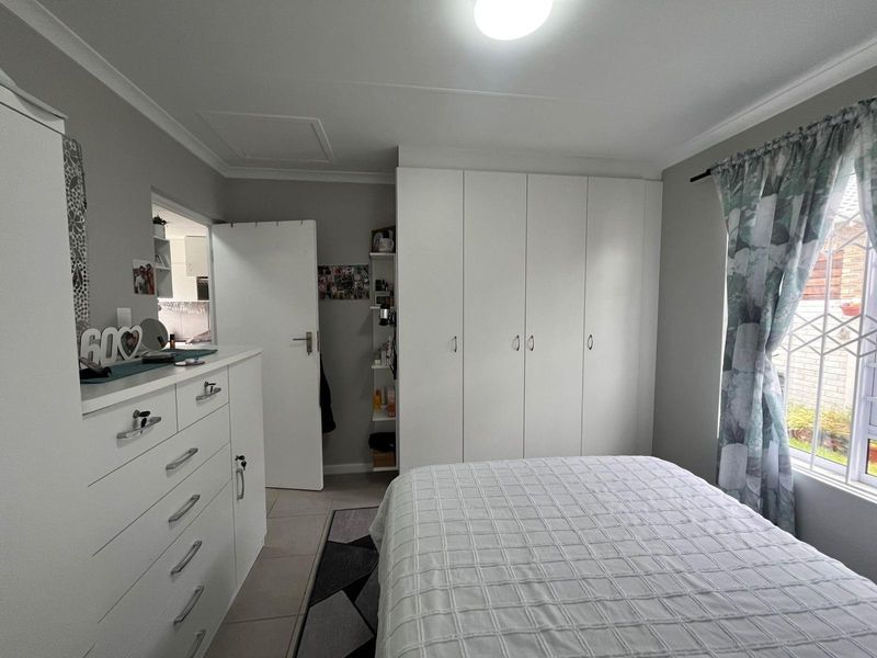 A well-maintained bedroom featuring built-in floor-to-ceiling wardrobes, tiled flooring, and a window with security bars.