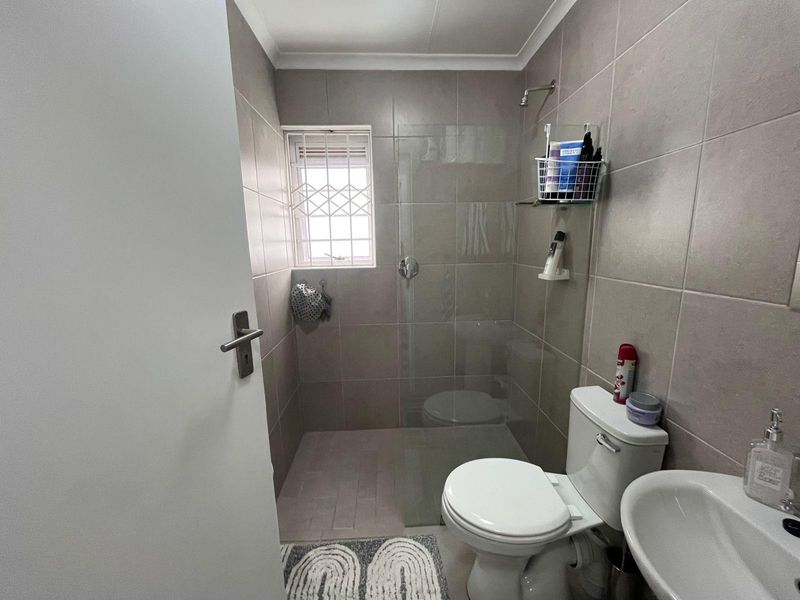 A compact bathroom featuring a walk-in shower with a glass screen, tiled walls, a toilet, and a pedestal basin.