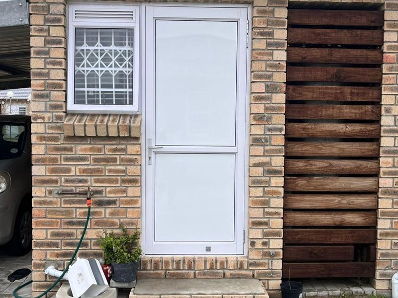 Exterior view of a townhouse entrance featuring face-brick facade, white aluminium door, security window grille, and a timber privacy screen.