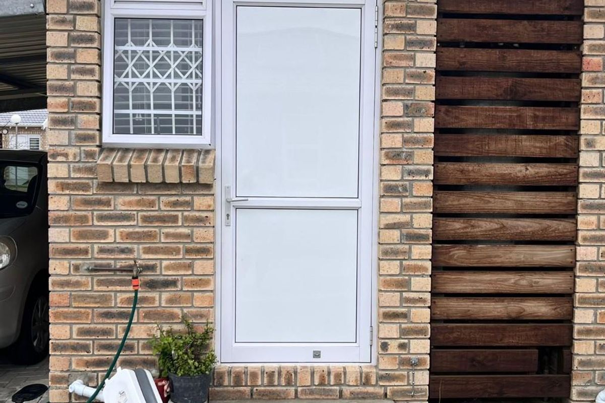Exterior view of a townhouse entrance featuring face-brick facade, white aluminium door, security window grille, and a timber privacy screen.