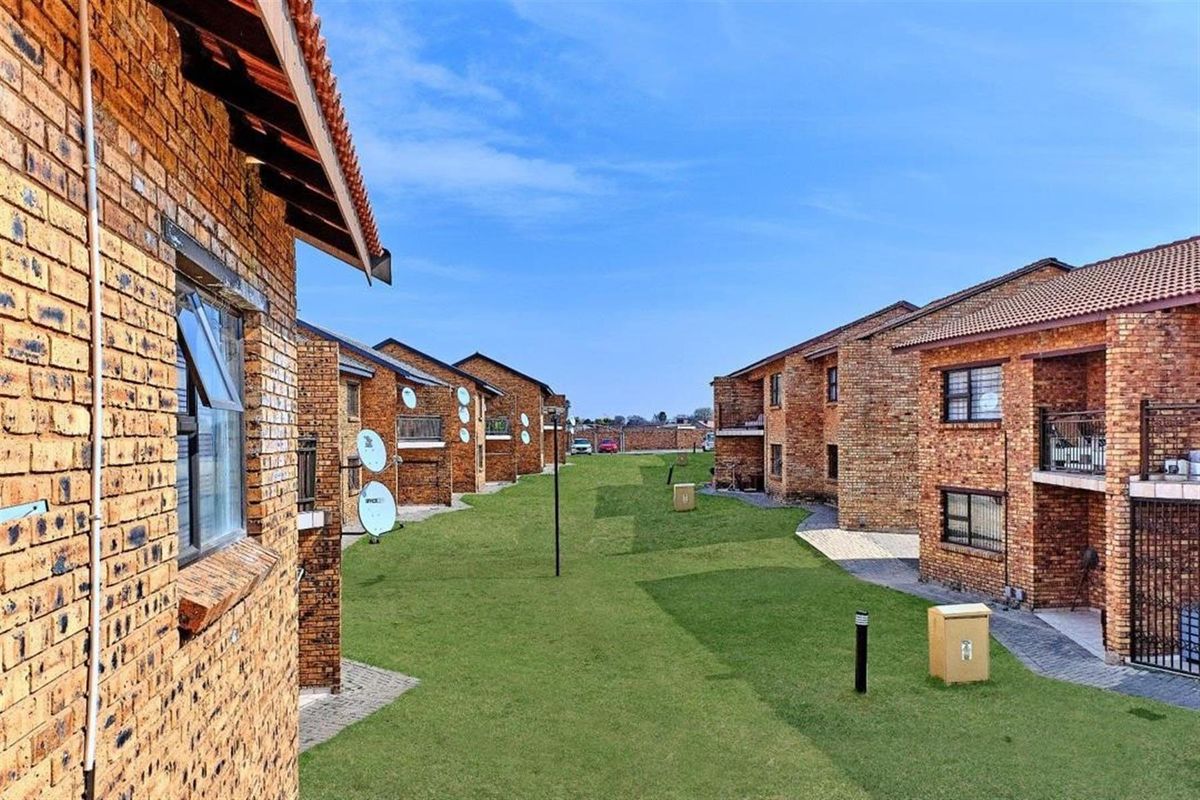 A view of the apartment complex grounds featuring face-brick building exteriors, manicured lawns, and paved walkways between the residential blocks.