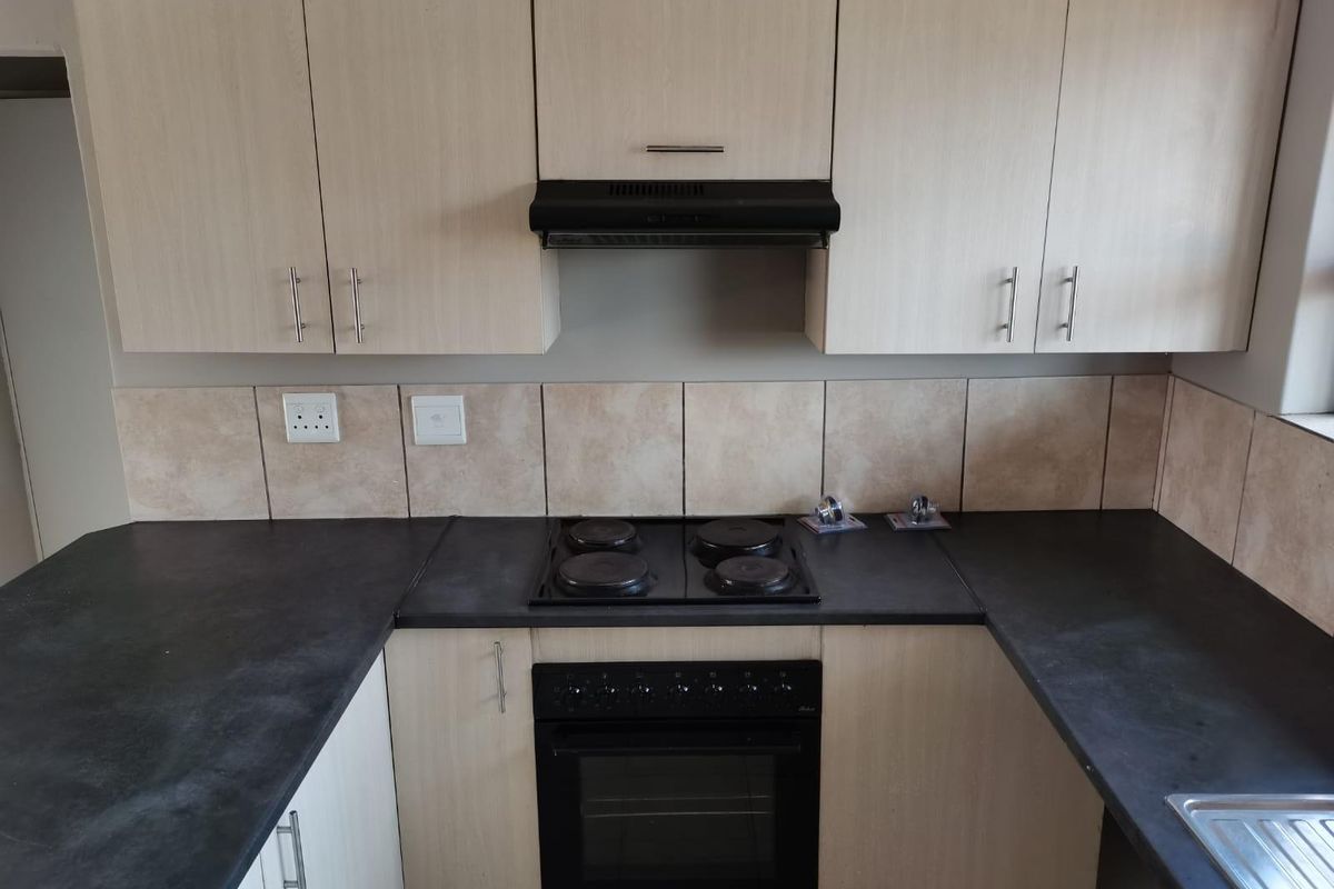 A functional kitchen featuring light wood-finish cabinetry, dark countertops, a built-in oven, electric hob, and an extractor fan with tiled splashbacks.