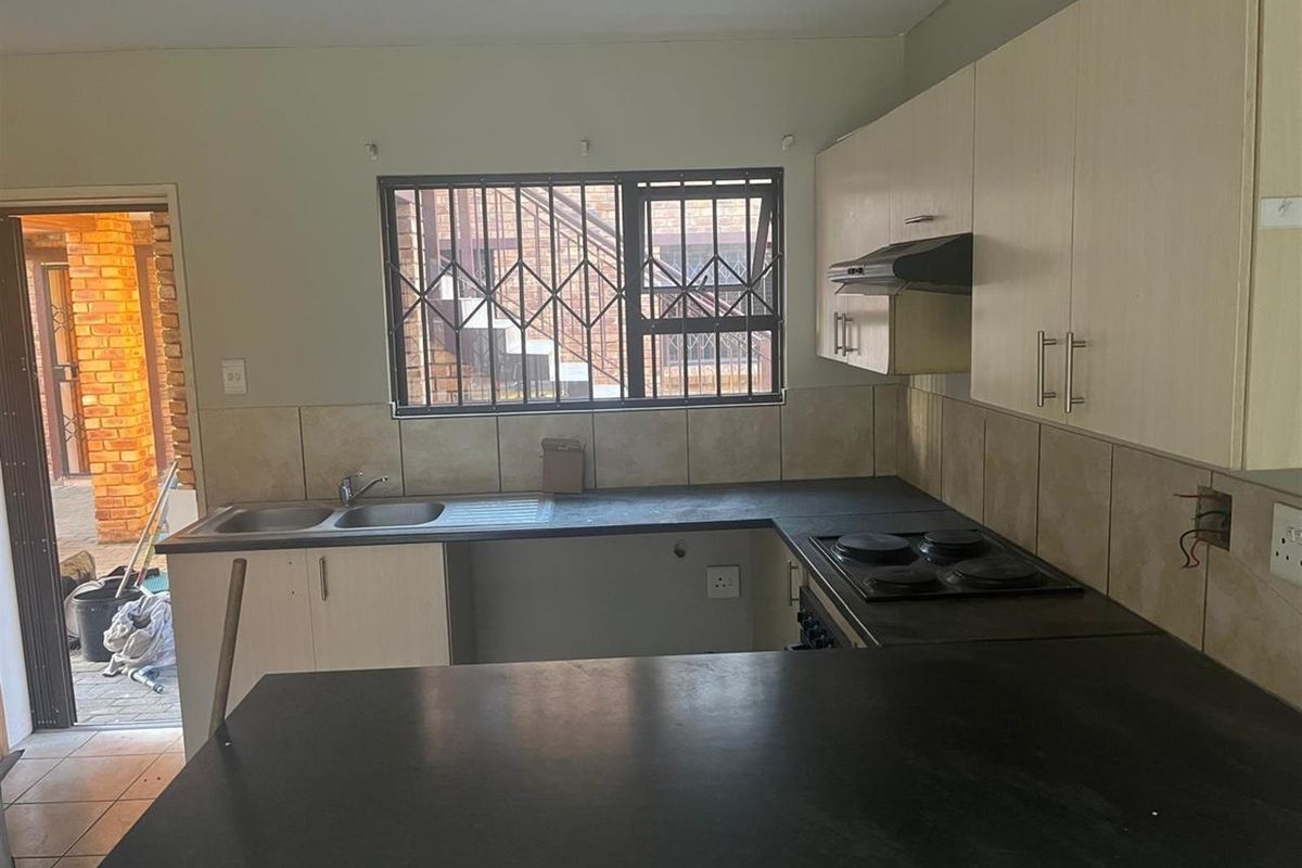 Functional kitchen featuring dark countertops, built-in hob, extractor fan, double sink, and light-toned cabinetry with direct access to an outdoor area.