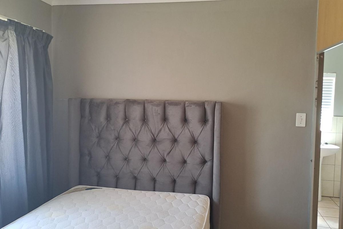 A bedroom featuring a tufted headboard and a view into an adjacent bathroom with tiled flooring.