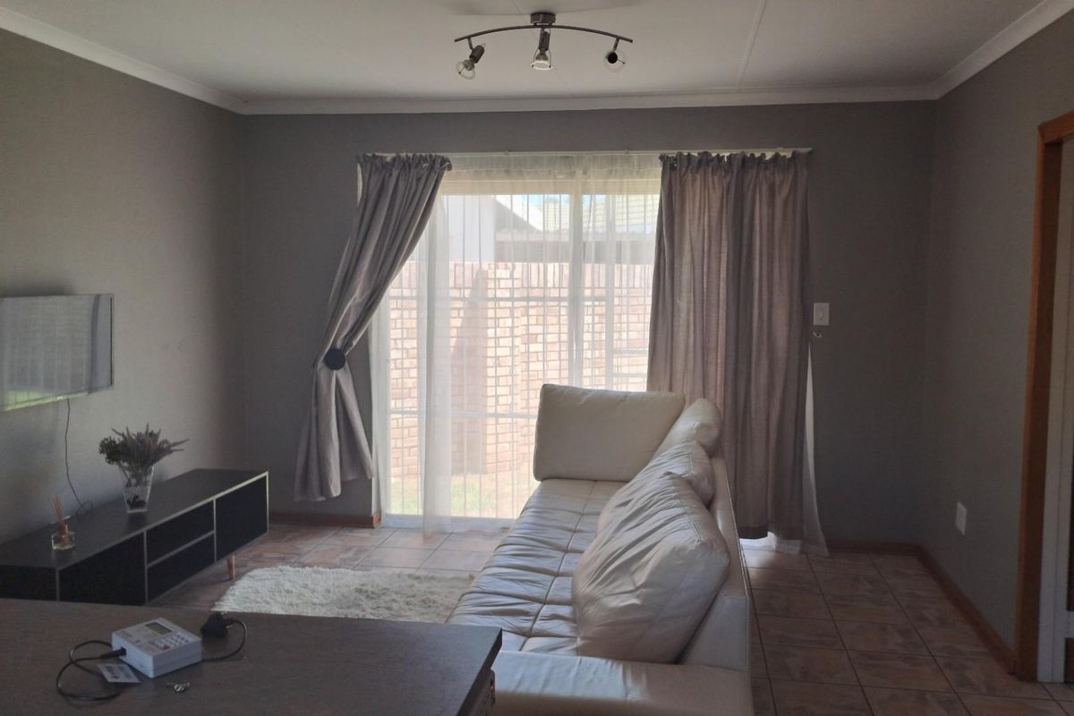 A living room featuring tiled flooring, a sliding glass door with curtains, and a ceiling-mounted spotlight fixture.