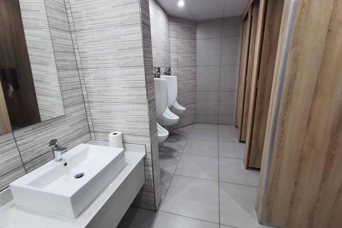 Modern commercial restroom featuring tiled walls, wall-mounted urinals, a sleek vanity with a vessel sink, and wooden stall partitions.