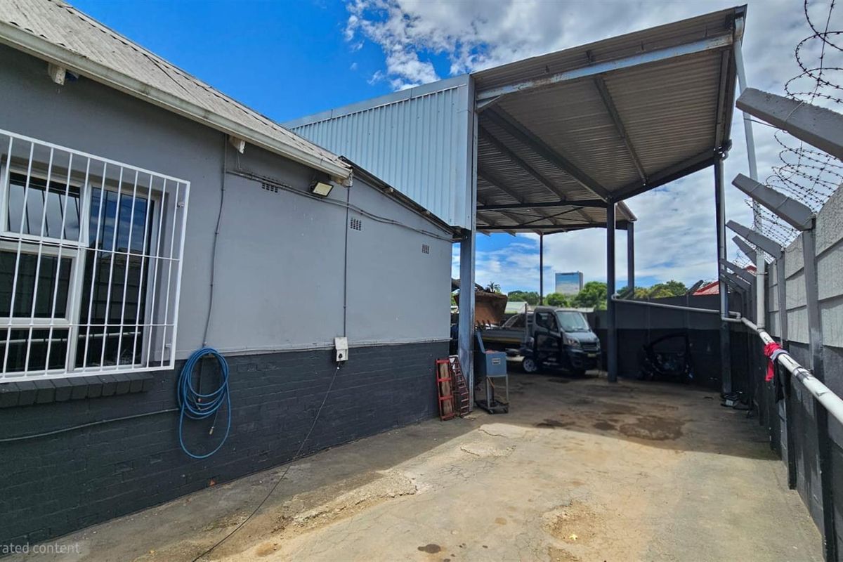 Exterior view of the office property featuring a covered parking or utility area with concrete flooring and perimeter security fencing.