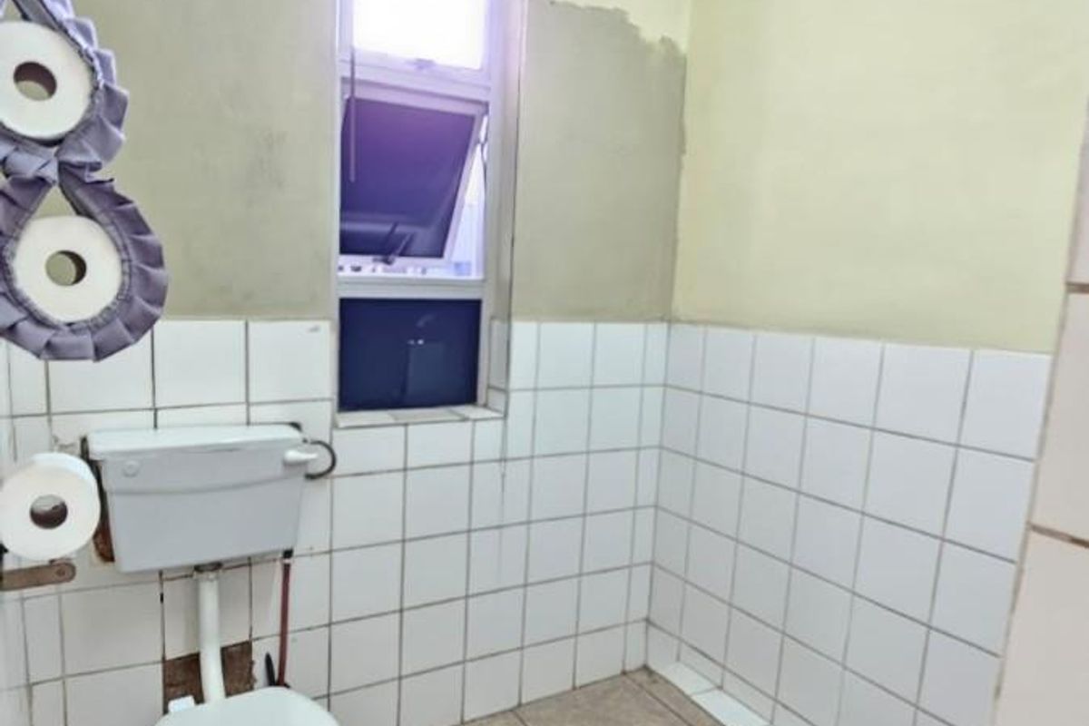 A small bathroom featuring a standard toilet, tiled flooring, and partially tiled walls requiring cosmetic repair and finishing.