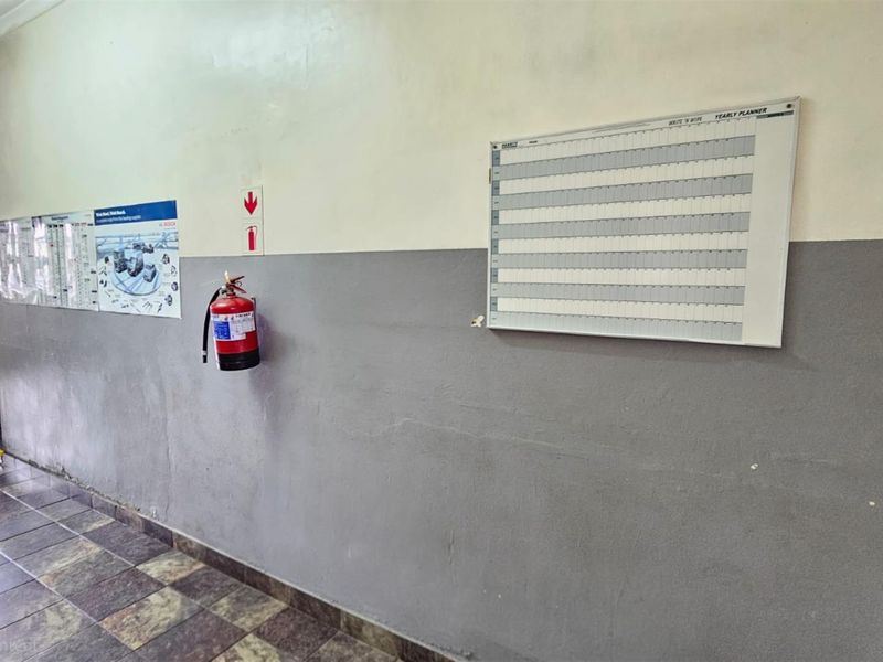 A functional office hallway featuring tiled flooring, two-tone painted walls, and mounted safety equipment including a fire extinguisher.