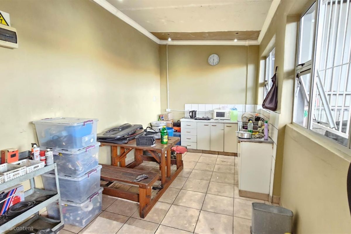 A functional office kitchenette area featuring basic cabinetry, tiled flooring, and large windows providing natural light.