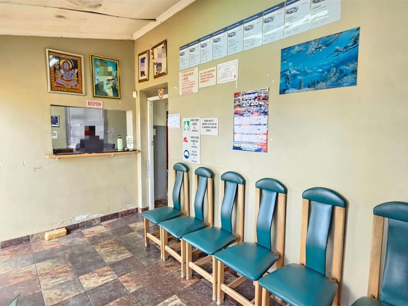 A waiting area in an office space featuring a reception window, tiled flooring, and wall-mounted signage.